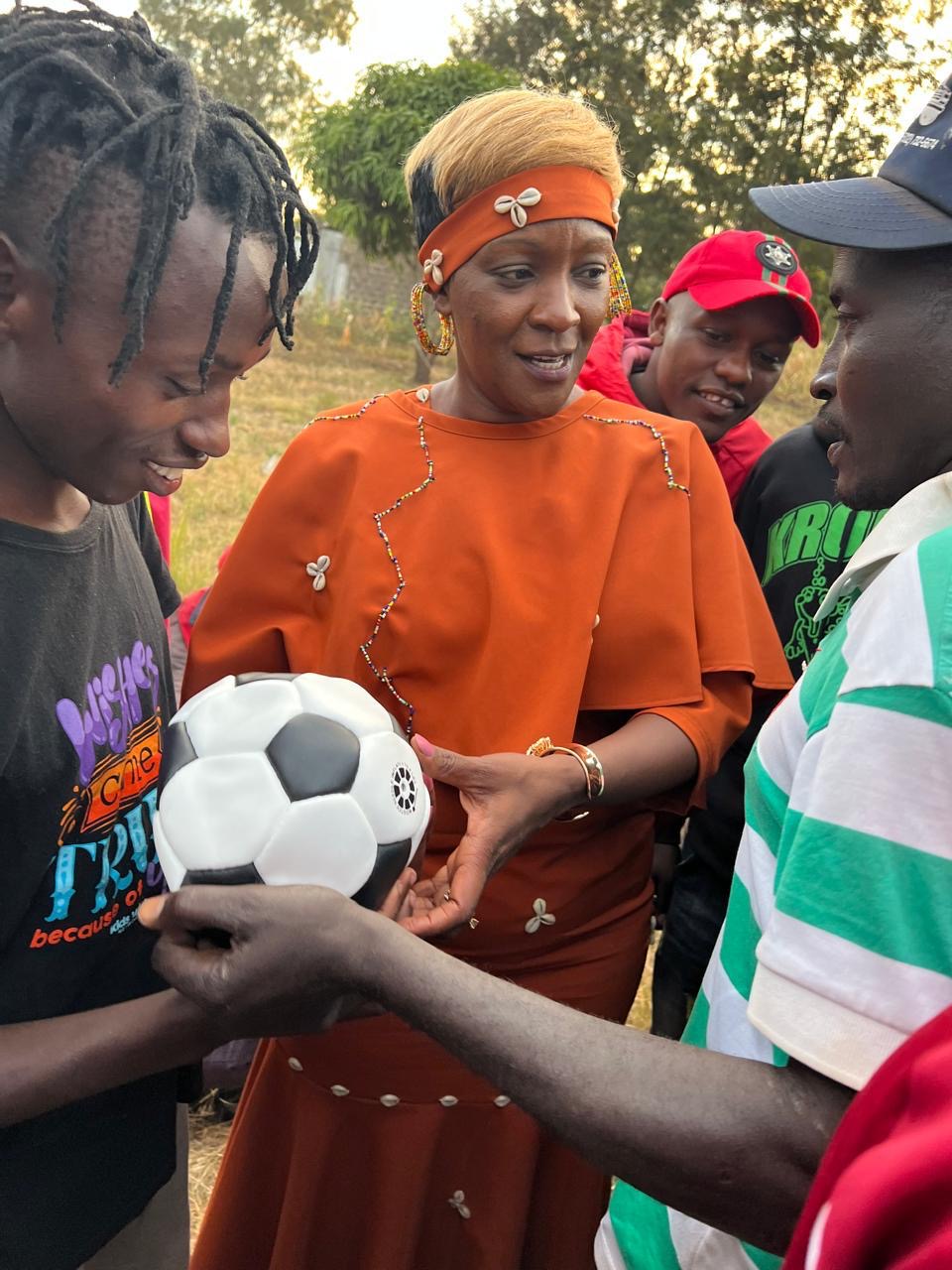 A woman handing a football to young men at a community youth event