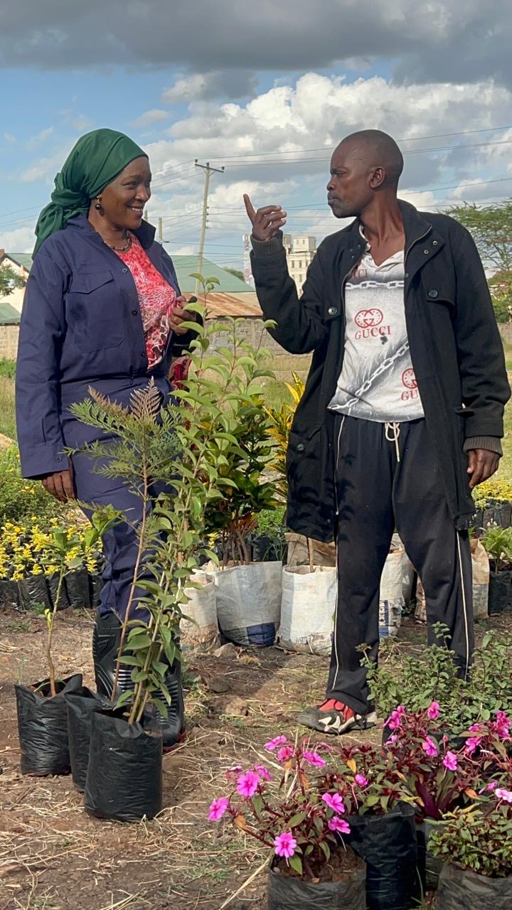 A woman in coveralls talking with a nursery worker among potted plants